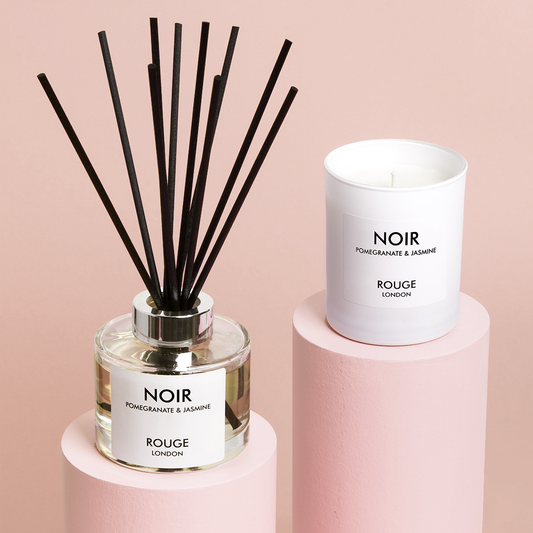 A luxury candle and diffuser set, with the candle labeled 'NOIR' and the diffuser labeled 'ROUGE LONDON', displayed on a pink surface.